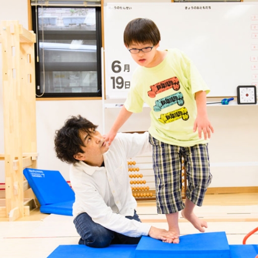 マットの上でバランスを取る子どもを講師が支えるトレーニングの様子