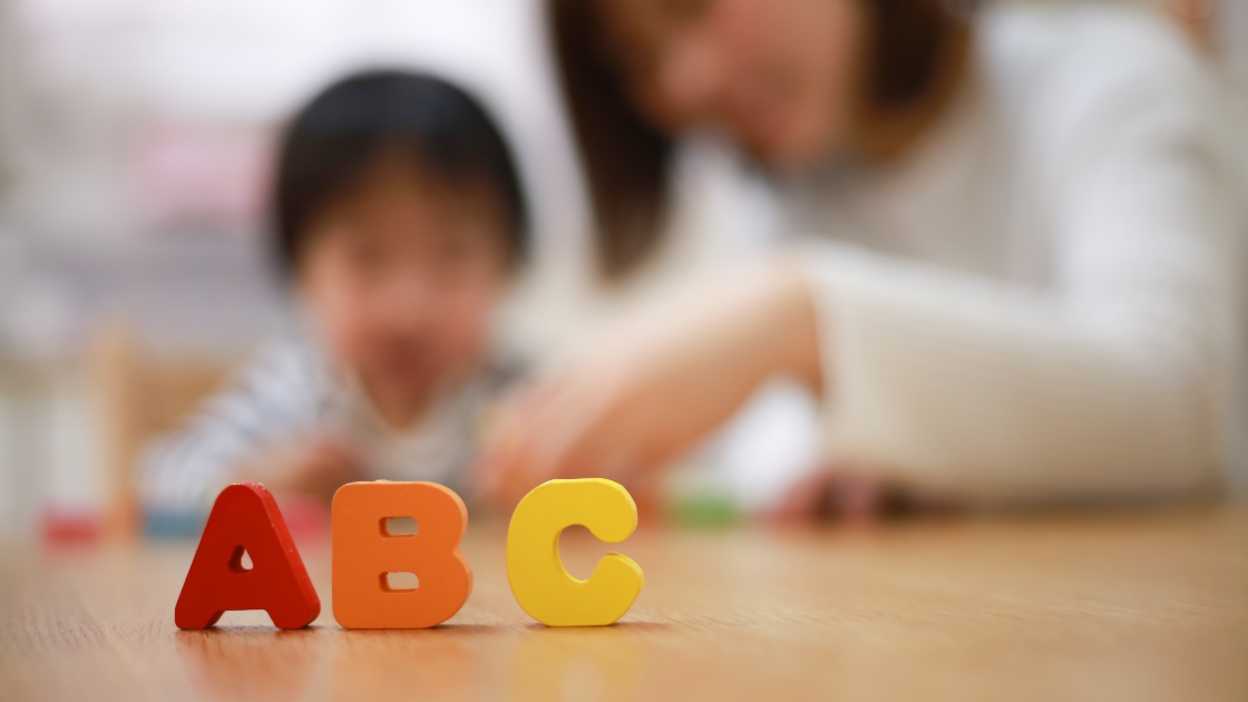 ABCのカラフルなブロックが置かれ、子どもと講師が遊んでいる様子の写真。