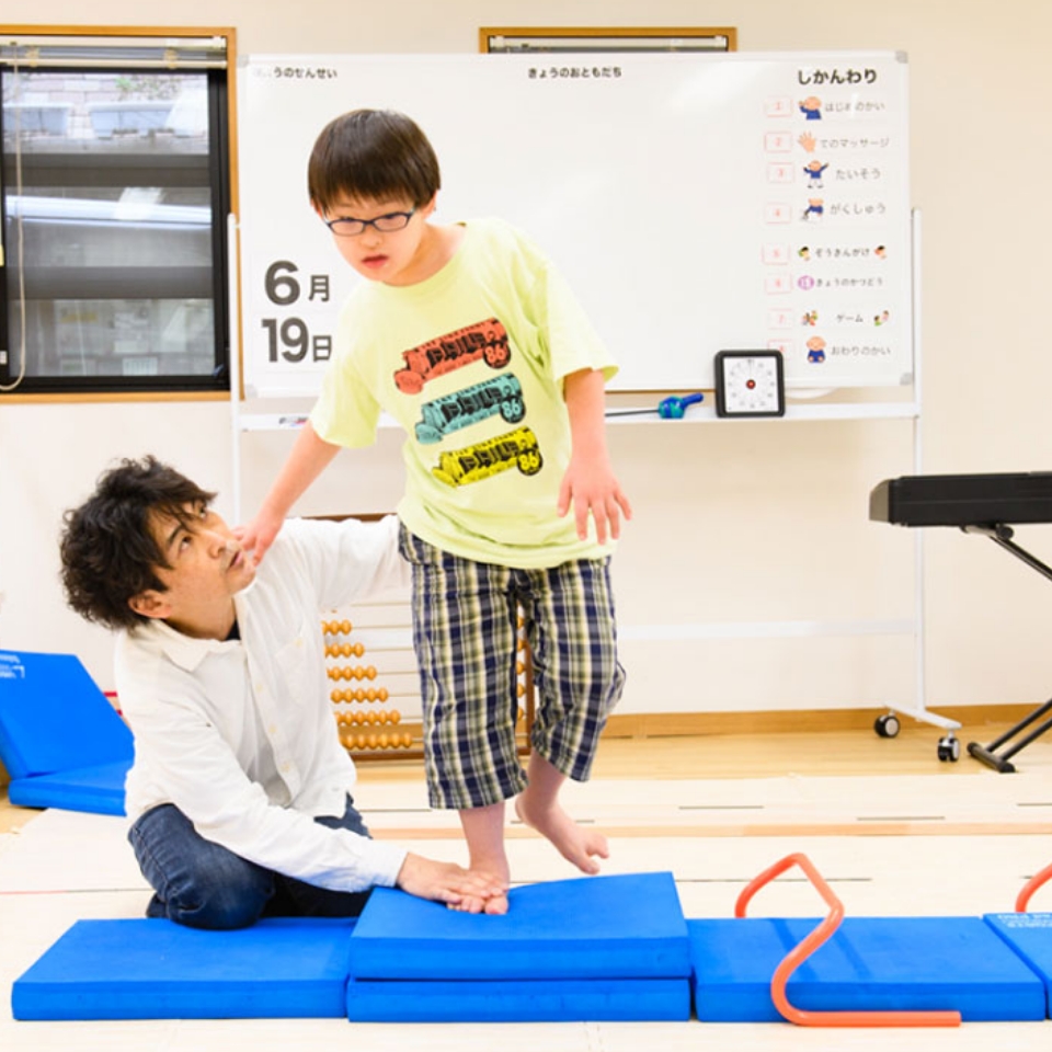マットの上でバランスを取る子どもを講師が支えるトレーニングの様子
