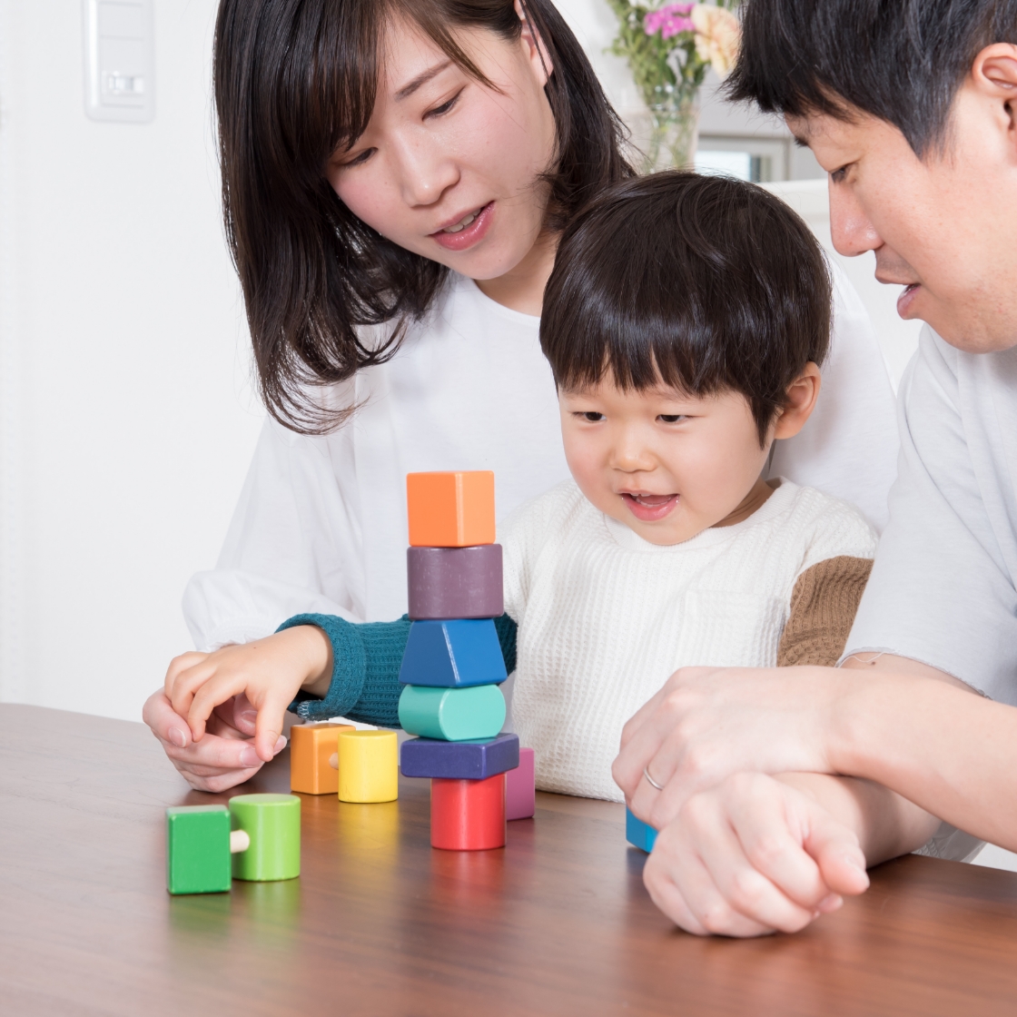 父親と母親が子どもを囲み一緒に積み木をしている様子
